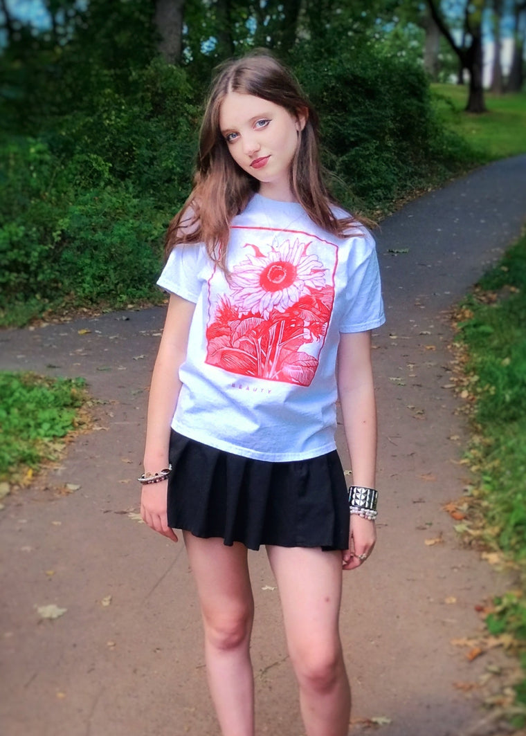 Young woman standing on a path in a park wearing a light blue t-shirt with a red graphic and black skirt.